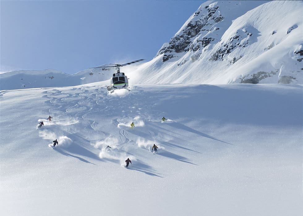 Skiers descending Panorama Mountain with a helicopter in the air above them